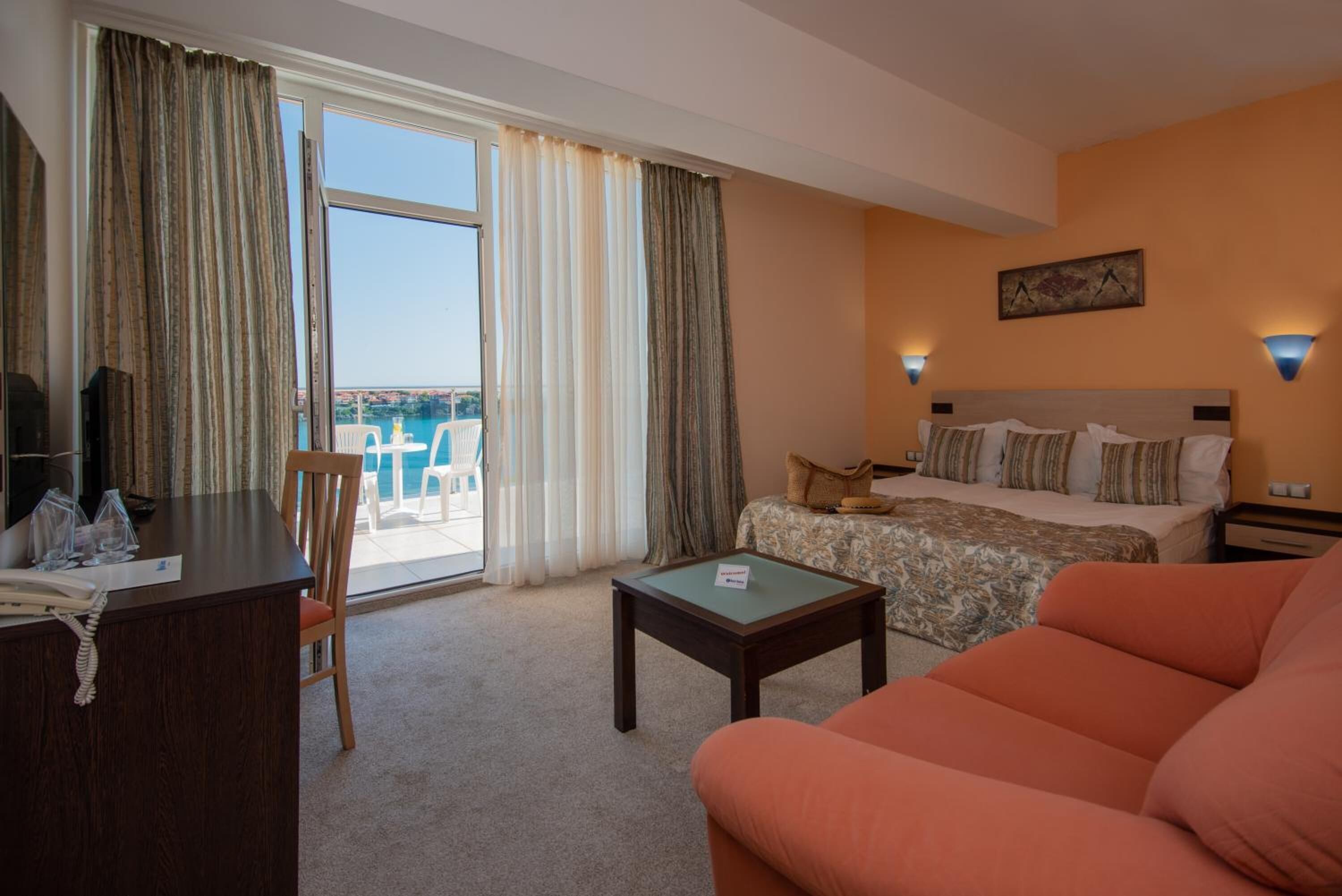 Ein Hotelzimmer mit Bett, einer Couch, einem Schreibtisch mit Telefon und Blick aufs Meer durch das Fenster.