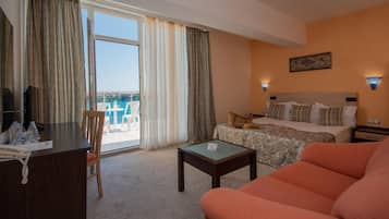 Ein Hotelzimmer mit Bett, einer Couch, einem Schreibtisch mit Telefon und Blick aufs Meer durch das Fenster.