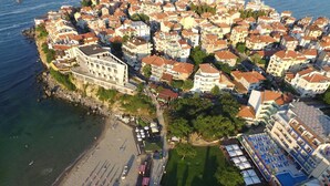 An aerial view of a coastal town with a beach, a large building with a white facade, and a densely packed area of residential buildings. - Selena (Sozopol)