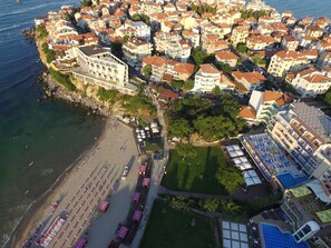 An aerial view of a coastal town with a beach, a large building with a white facade, and a densely packed area of residential buildings. - Selena (Sozopol)