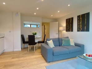 A modern living room with a grey sofa, a dining table with chairs, and a small table with apples. - Your Space Apartments - Cambridge Place (Cambridge)