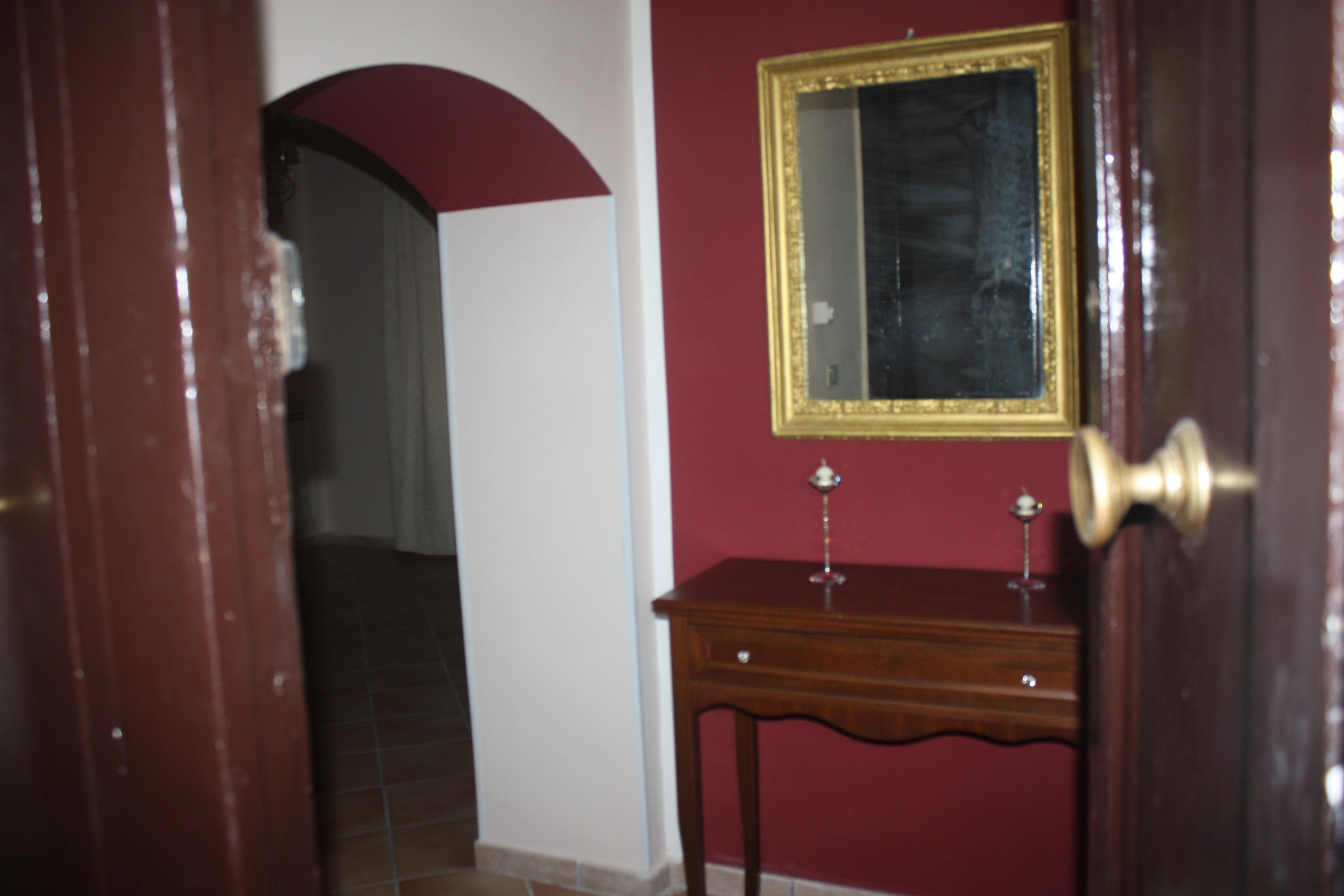 A doorway leading to a room with a red wall, a mirror with a gold frame, and a wooden cabinet.