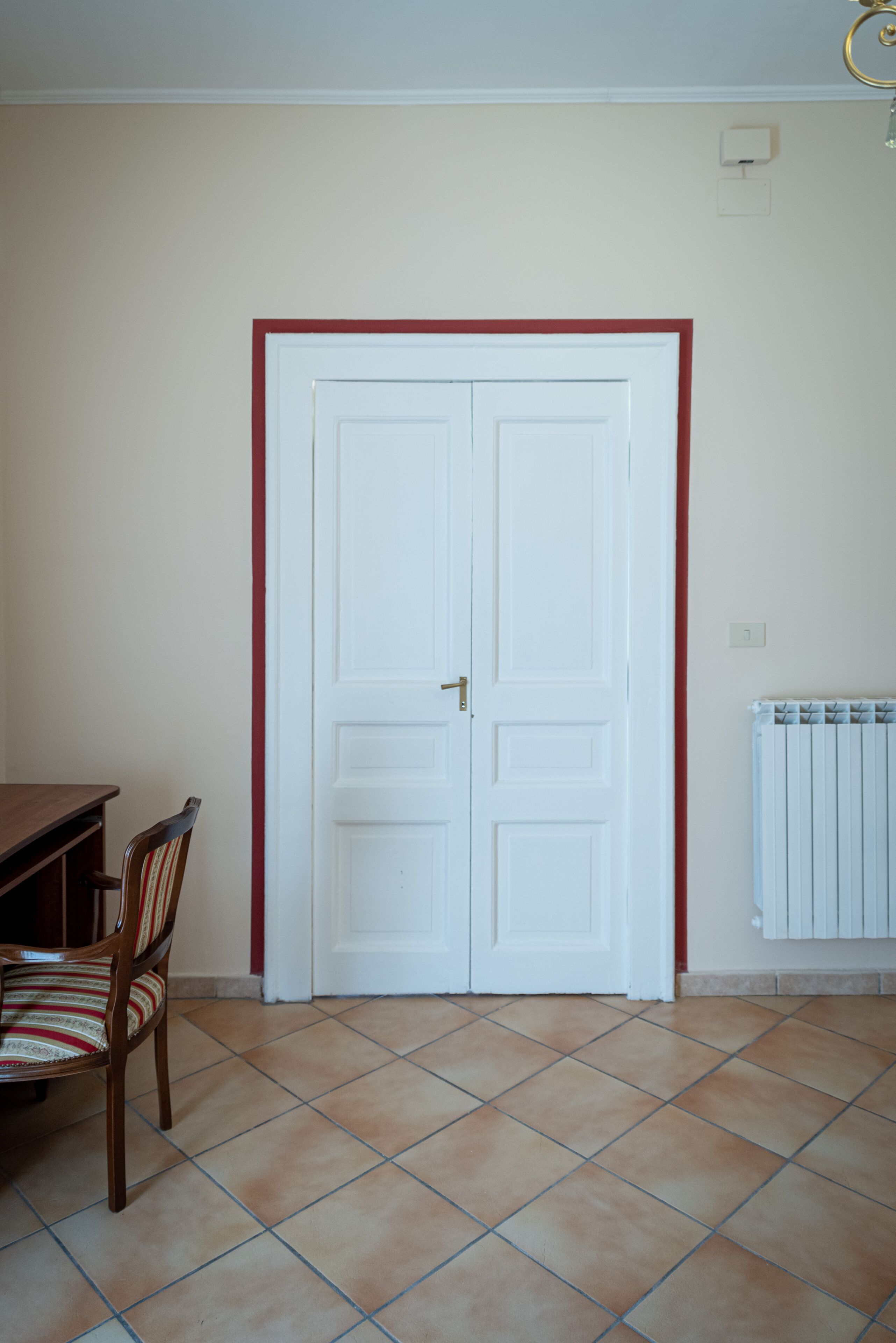 Une pièce dotée d’une double porte, d’un radiateur, d’une chaise en bois et d’un sol carrelé.