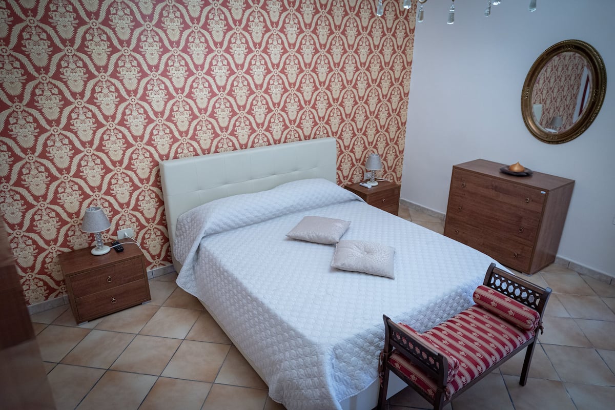 Un lit bien fait, avec des oreillers, une table de chevet avec une lampe, une petite table en bois et une commode.