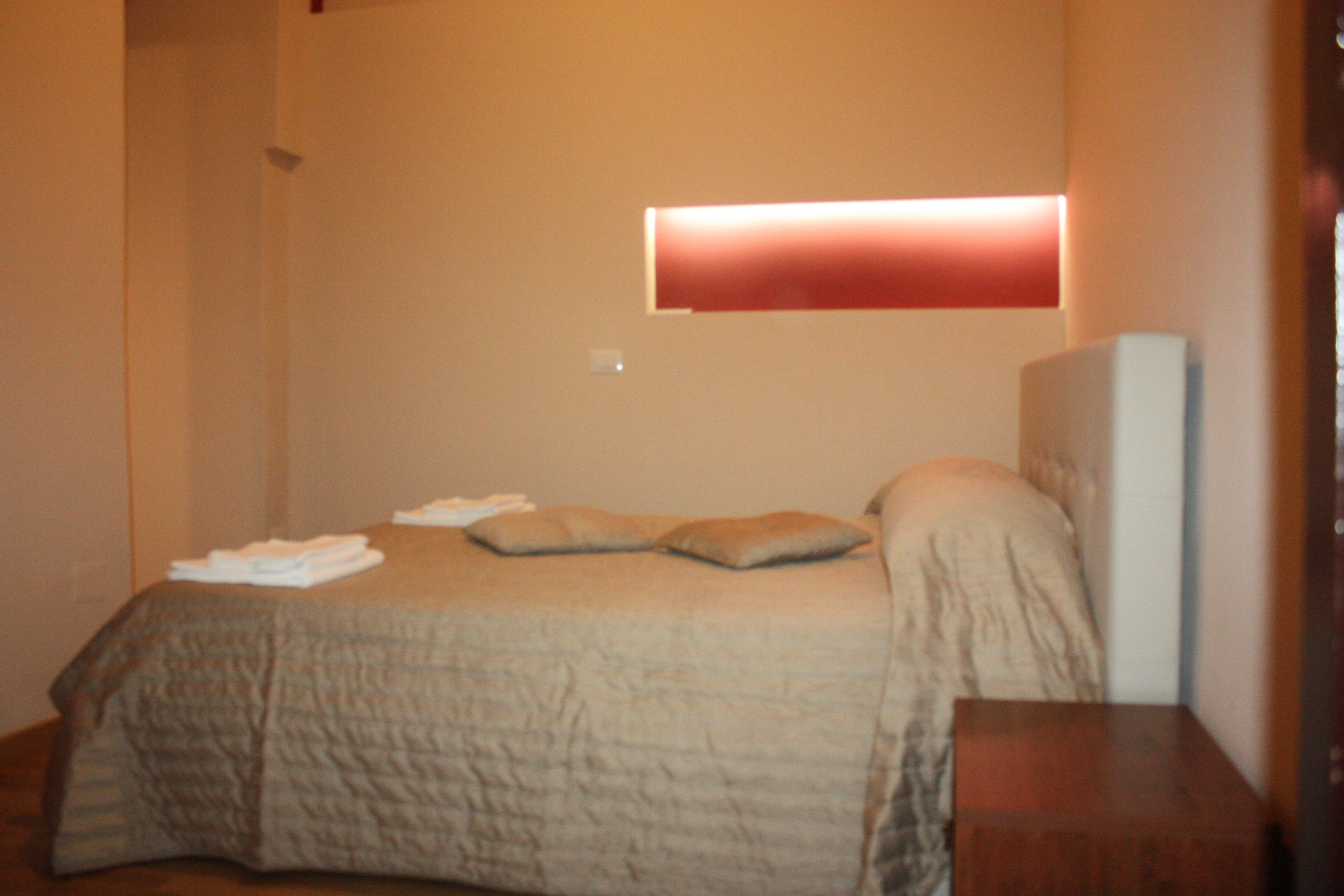 A bedroom with a bed, pillows, a bedside table, and a wall-mounted light fixture.