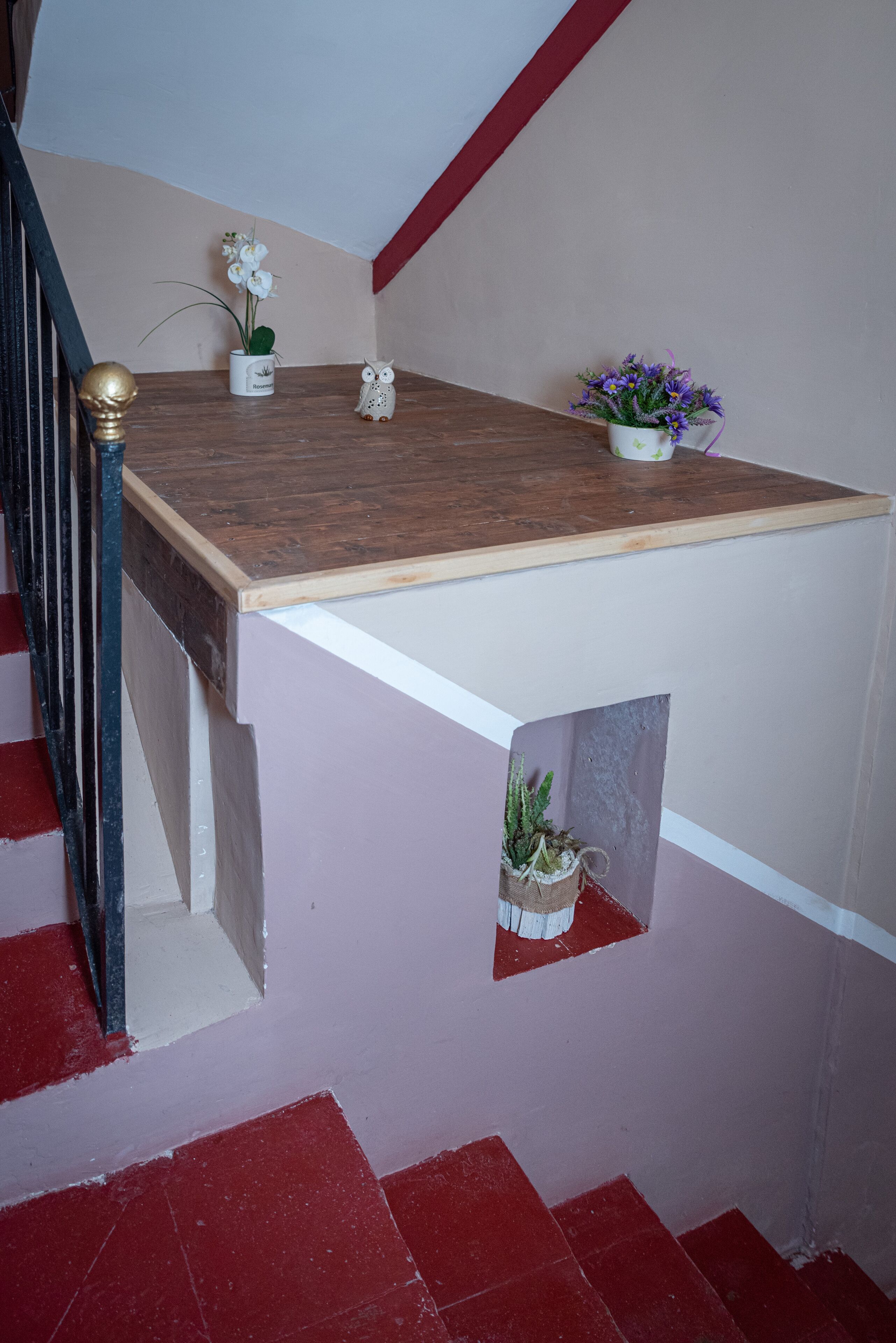 Eine Treppe mit einem Holzgeländer, einer weißen Wand und einem roten Fliesenboden.