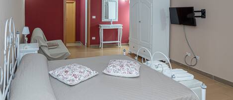 Un dormitorio con cama, tocador, armario y televisor montado en la pared.