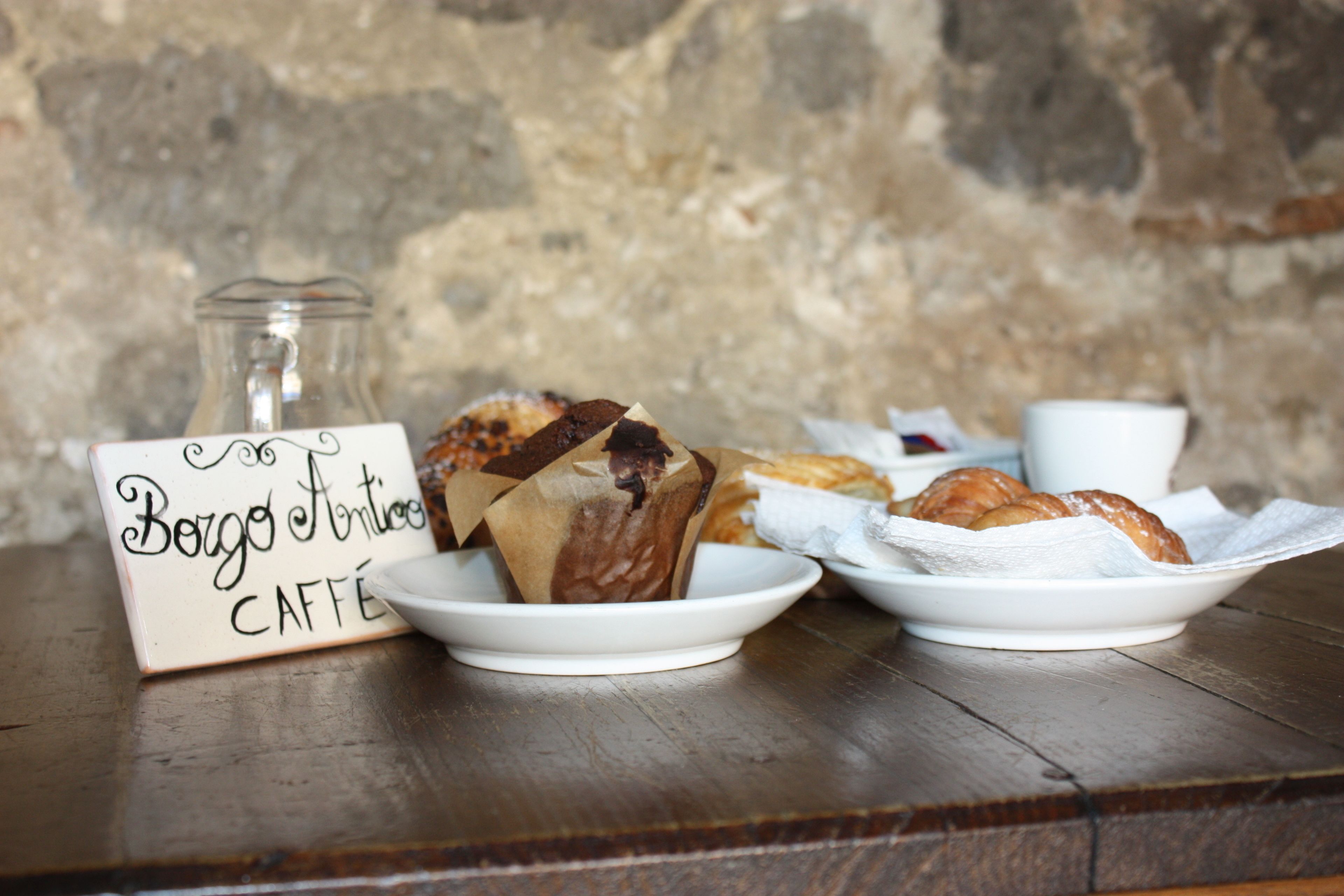 A rustic wooden table with a sign reading "Berg Antico Caffè," a glass jar, and pastries on white plates.