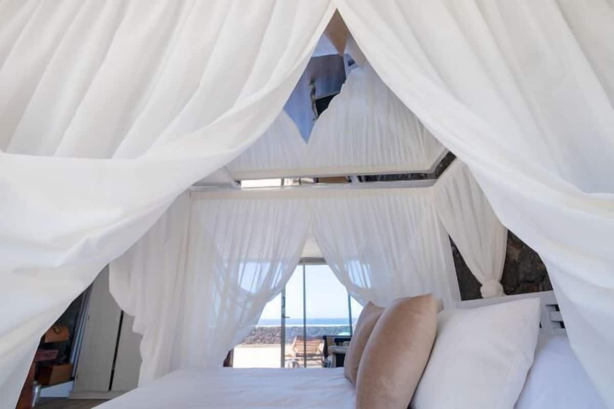 A bedroom with a bed, white curtains, and a view of the outdoors.