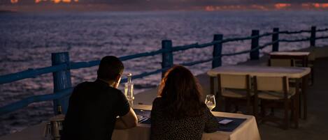 A couple dining at a table with a view of the ocean and sunset.