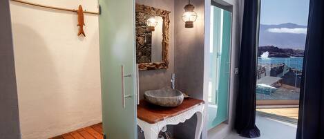 Un baño con suelo de madera, lavamanos de piedra y un espejo grande con marco rústico.