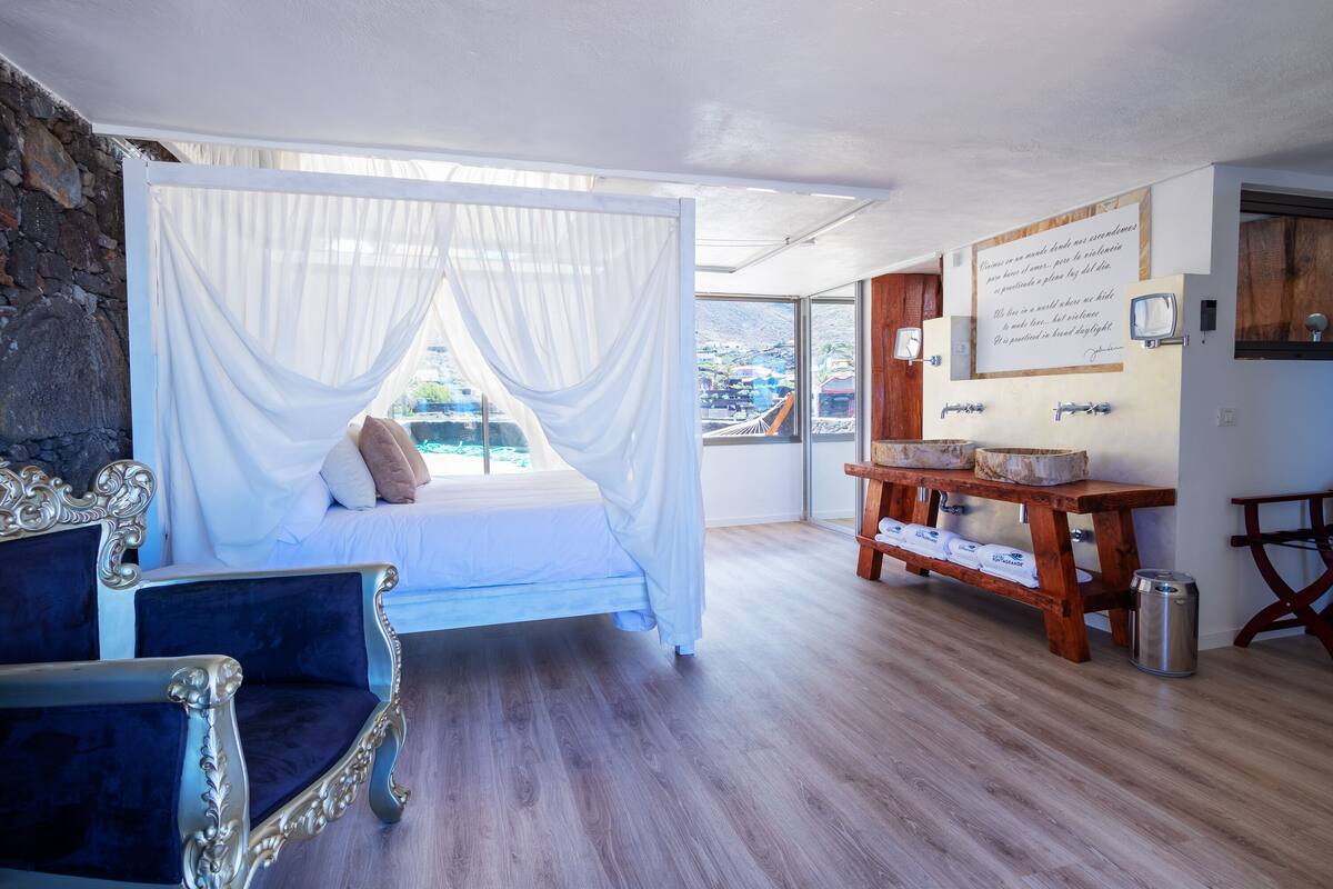 A bedroom with a canopy bed, a wooden table with towels, and a view of the city.