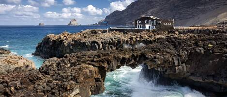 A coastal building with a rocky shoreline, waves crashing against the rocks, and a clear view of the sea.