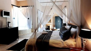 A hotel room with a bed, a TV, a desk, and a window with curtains. - Villa Paradiso Country Manor (Hartbeespoort)