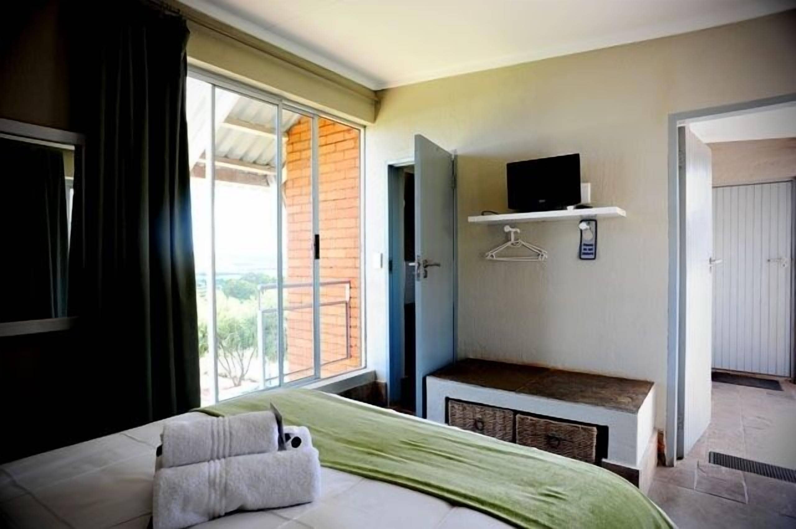 Quarto com uma cama, uma TV em uma estante, janela com cortinas e porta que dá para uma área externa.