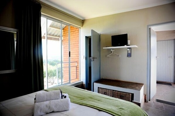 Quarto com uma cama, uma TV em uma estante, janela com cortinas e porta que dá para uma área externa.