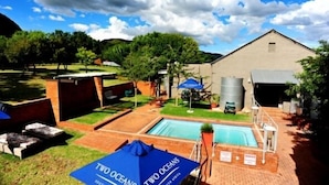 A pool area with a building, outdoor seating, and a sign for "Two Oceans". - Villa Paradiso Country Manor (Hartbeespoort)