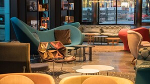 A modern lounge area with sofas, chairs, and tables, featuring a large window with a view of the city. - Motel One Berlin-Alexanderplatz (Berlin)