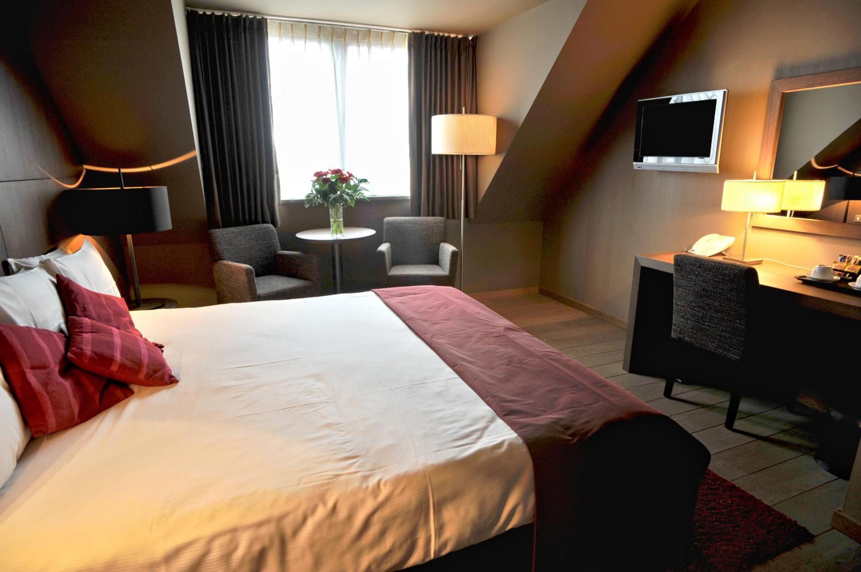A hotel room with a large bed, a desk, a chair, a TV, and a window with curtains.