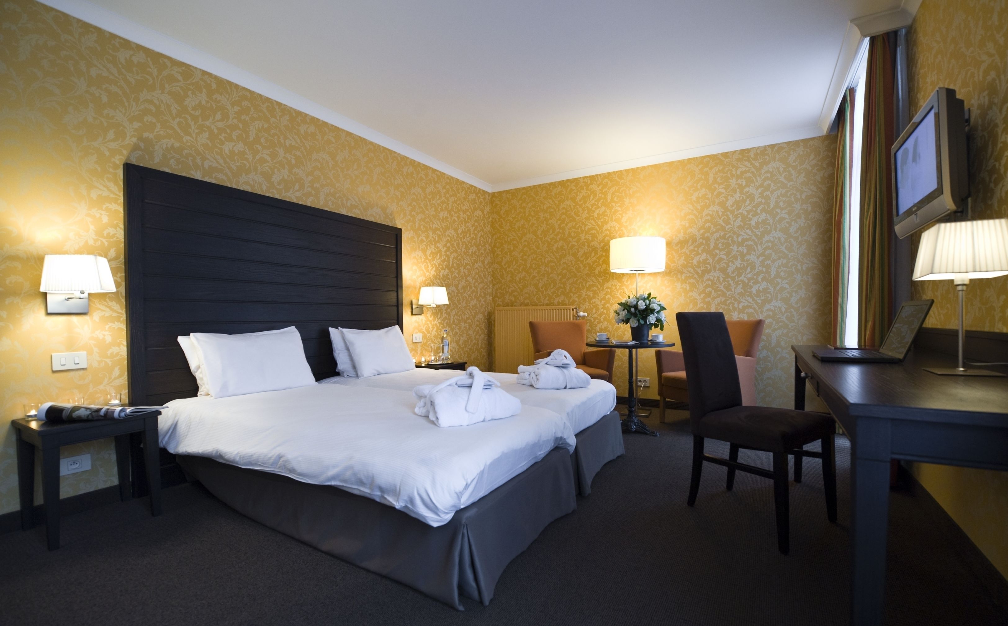 A hotel room with a large bed, two bedside tables, a desk, a chair, and a TV.
