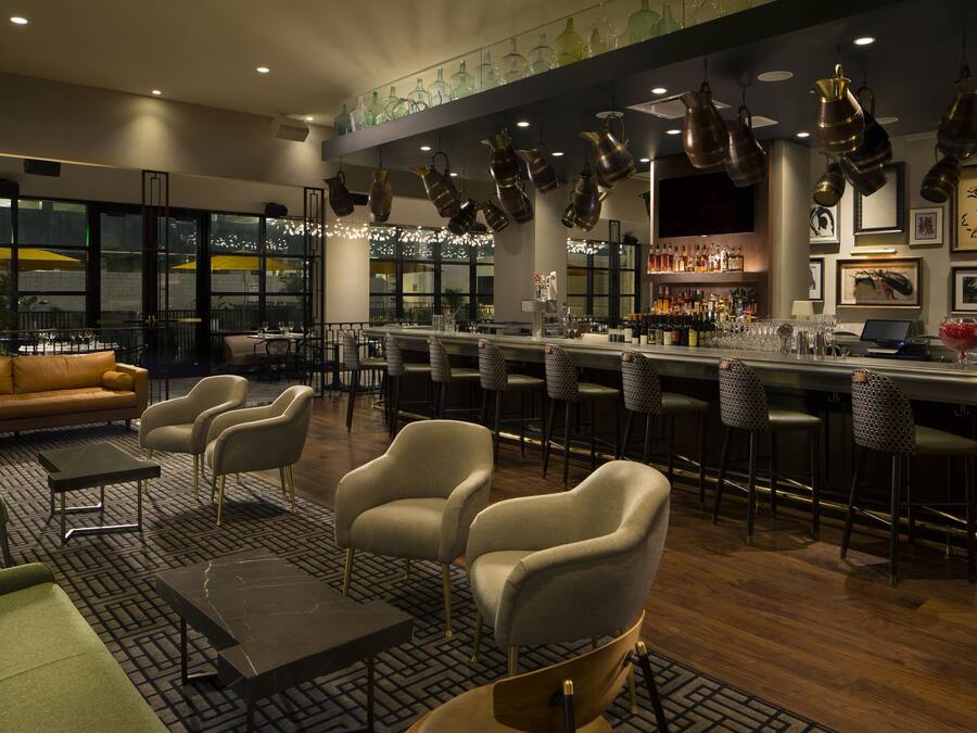 A modern bar area with a bar counter, seating, and a view of the cityscape.
