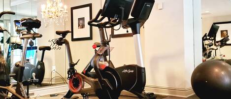 Ein Heimfitnessraum mit Crosstrainer, Ergometer und einer großen Trainingsbank.