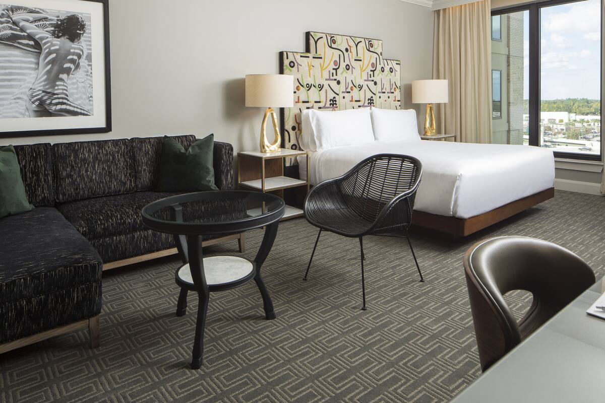 A hotel room with a bed, a sofa, a chair, a small table, and a painting on the wall.