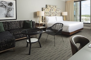 A hotel room with a bed, a sofa, a chair, a small table, and a painting on the wall.