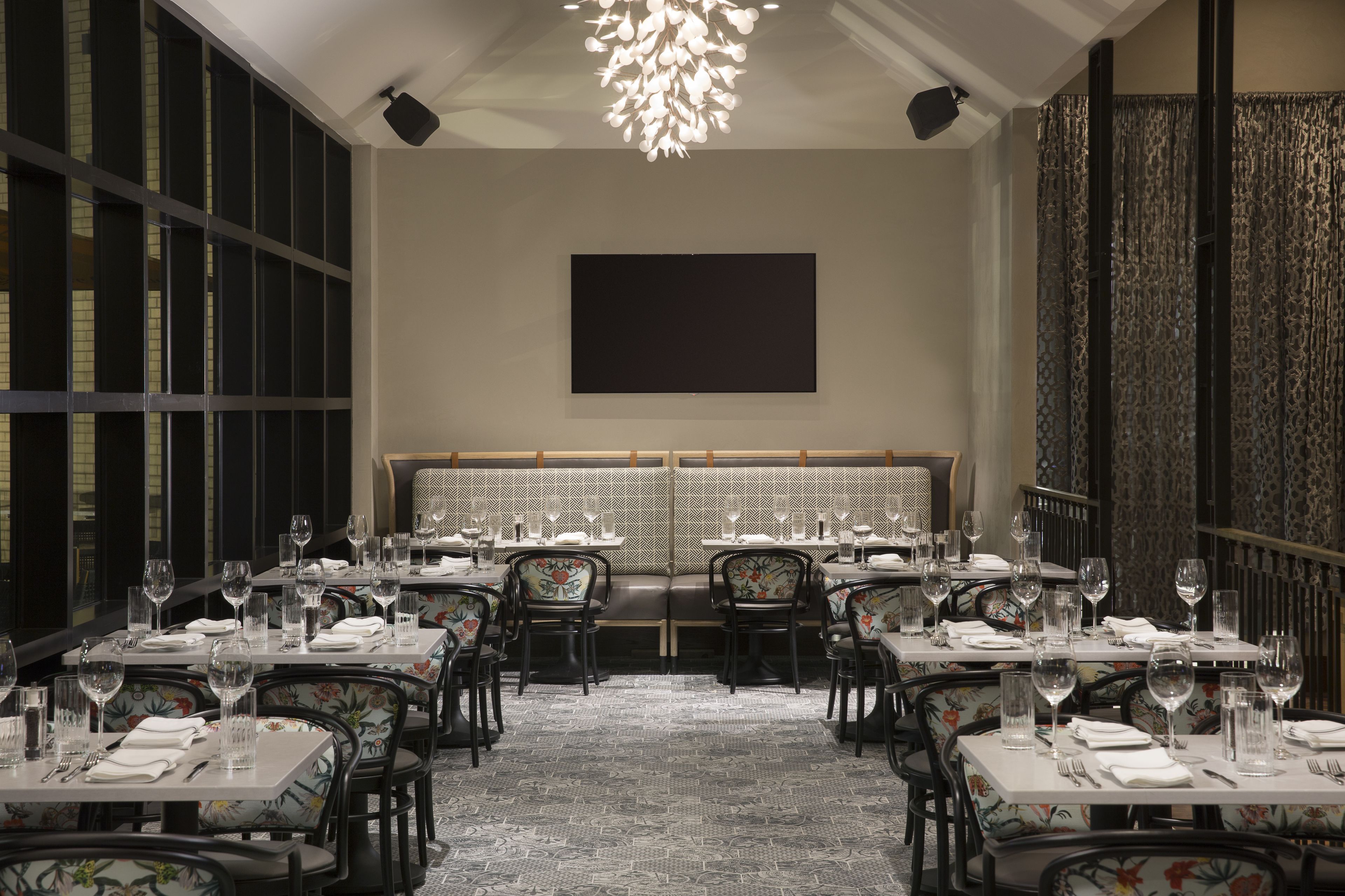 A restaurant with tables set for dining, a large chandelier, and a patterned wall.
