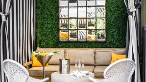 A cozy seating area with a cushioned sofa, two wicker chairs, a round table, and a decorative wall with a geometric pattern. - Hotel ZaZa Houston Memorial City (Houston)