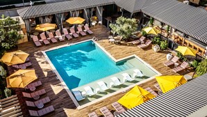 Un área de piscina en la azotea con múltiples sillones de descanso y sombrillas, rodeada de cubierta de madera y plantas en macetas.
