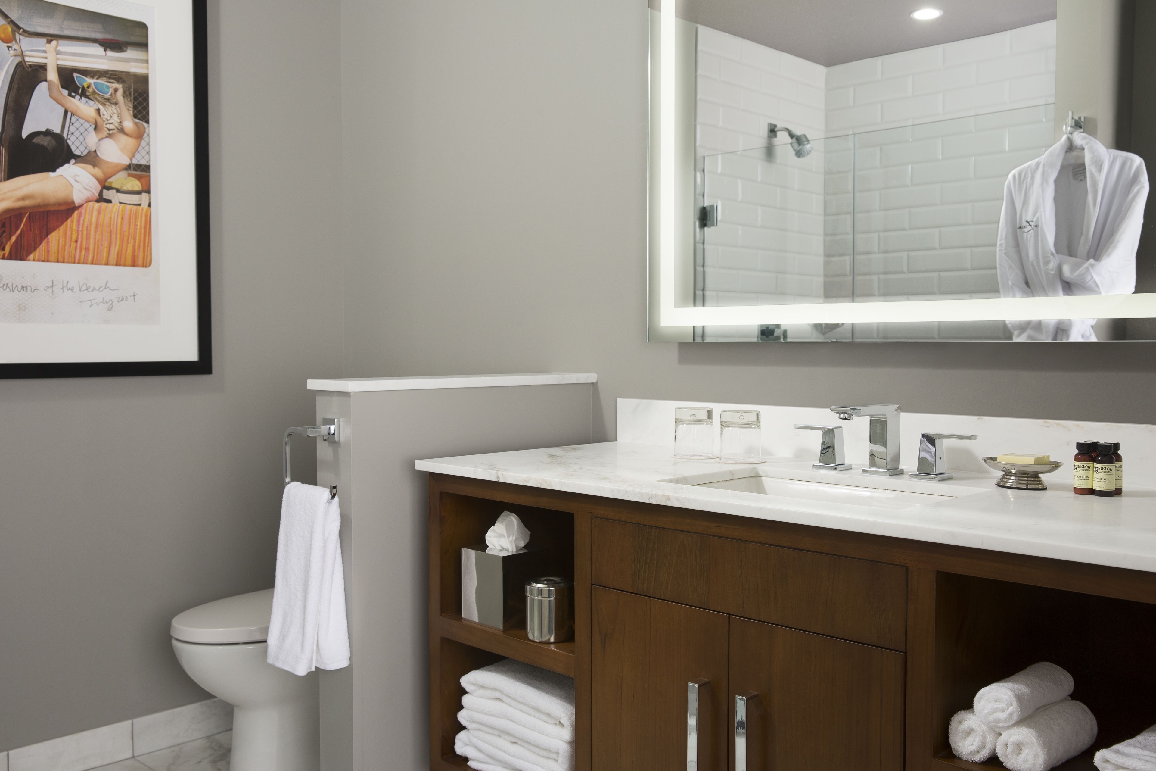A modern bathroom with a white sink, mirror, and toilet. There are towels and toiletries on the counter.