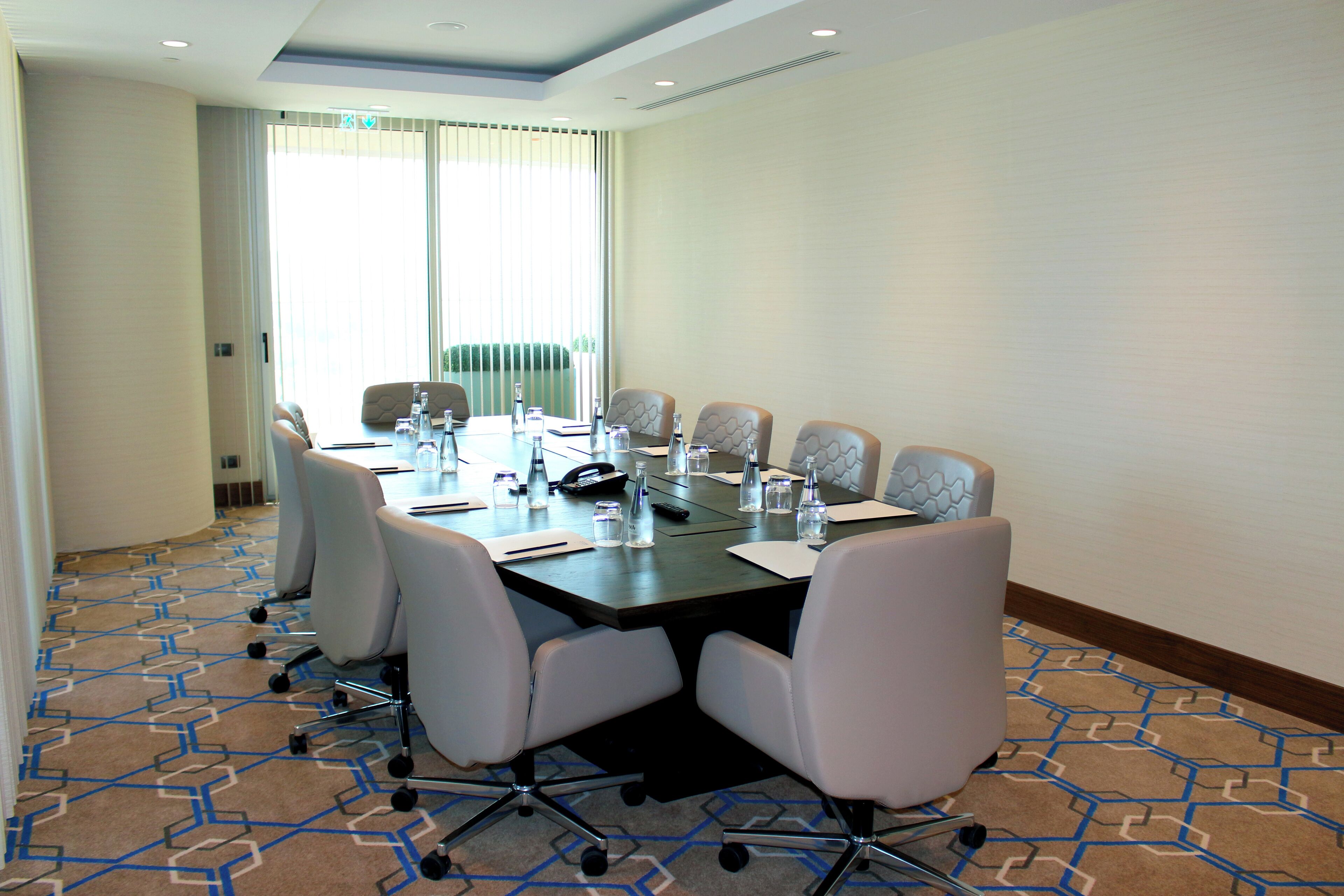 Un salón de conferencias con una larga mesa, sillas blancas y piso alfombrado.