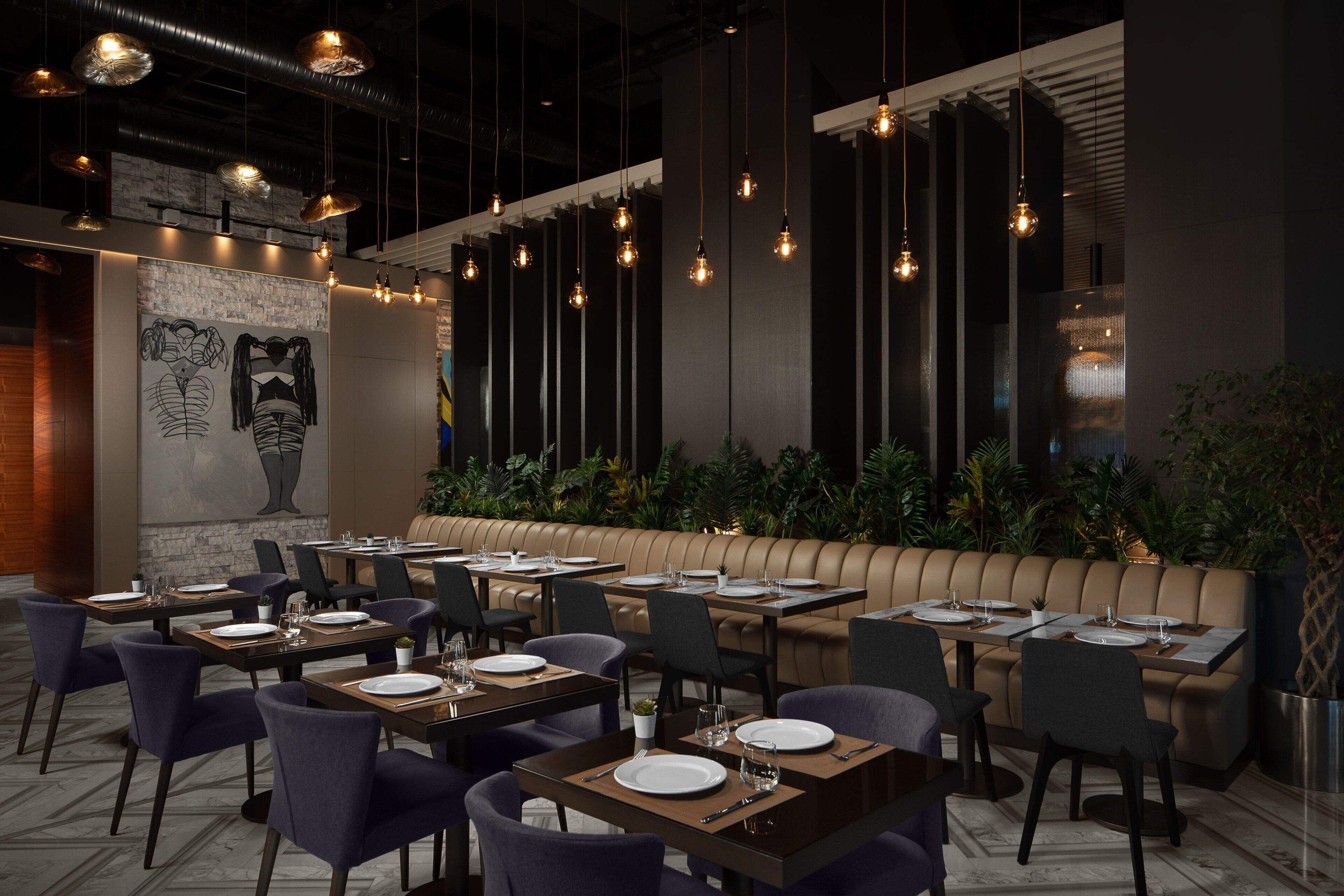 A restaurant with multiple tables and booths, hanging pendant lights, and a mural on the wall.