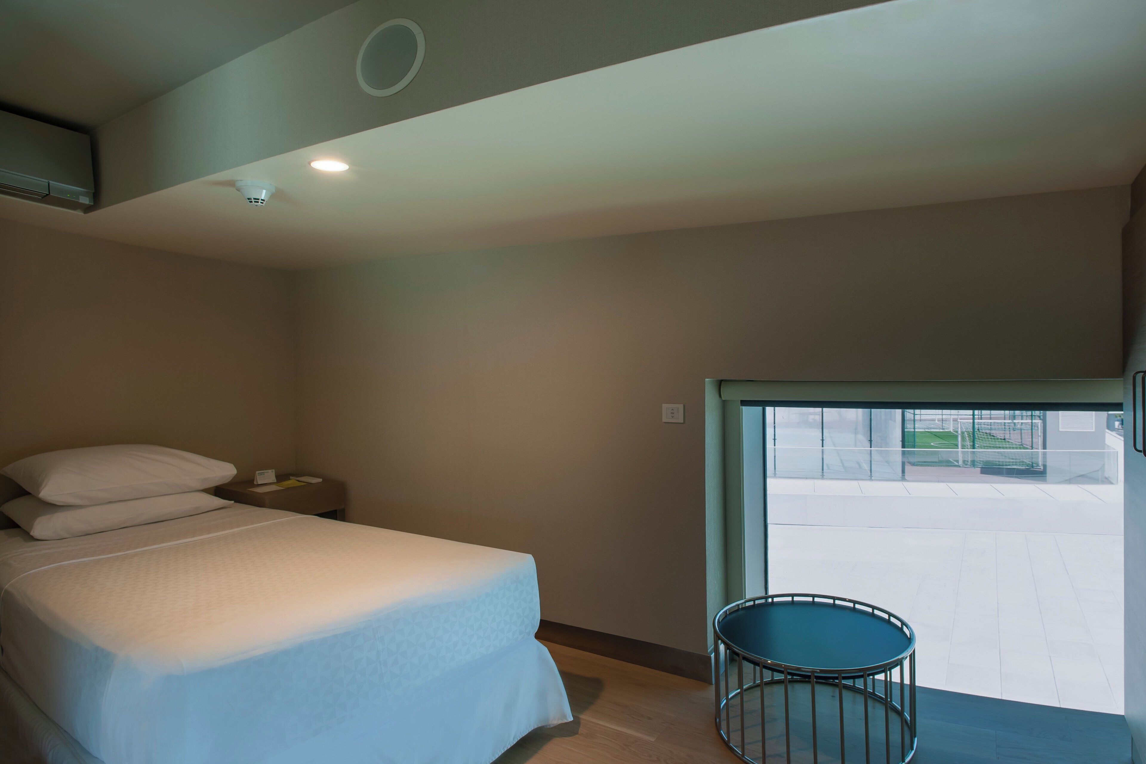 A hotel room with a bed, a small table, and a view of the outside.