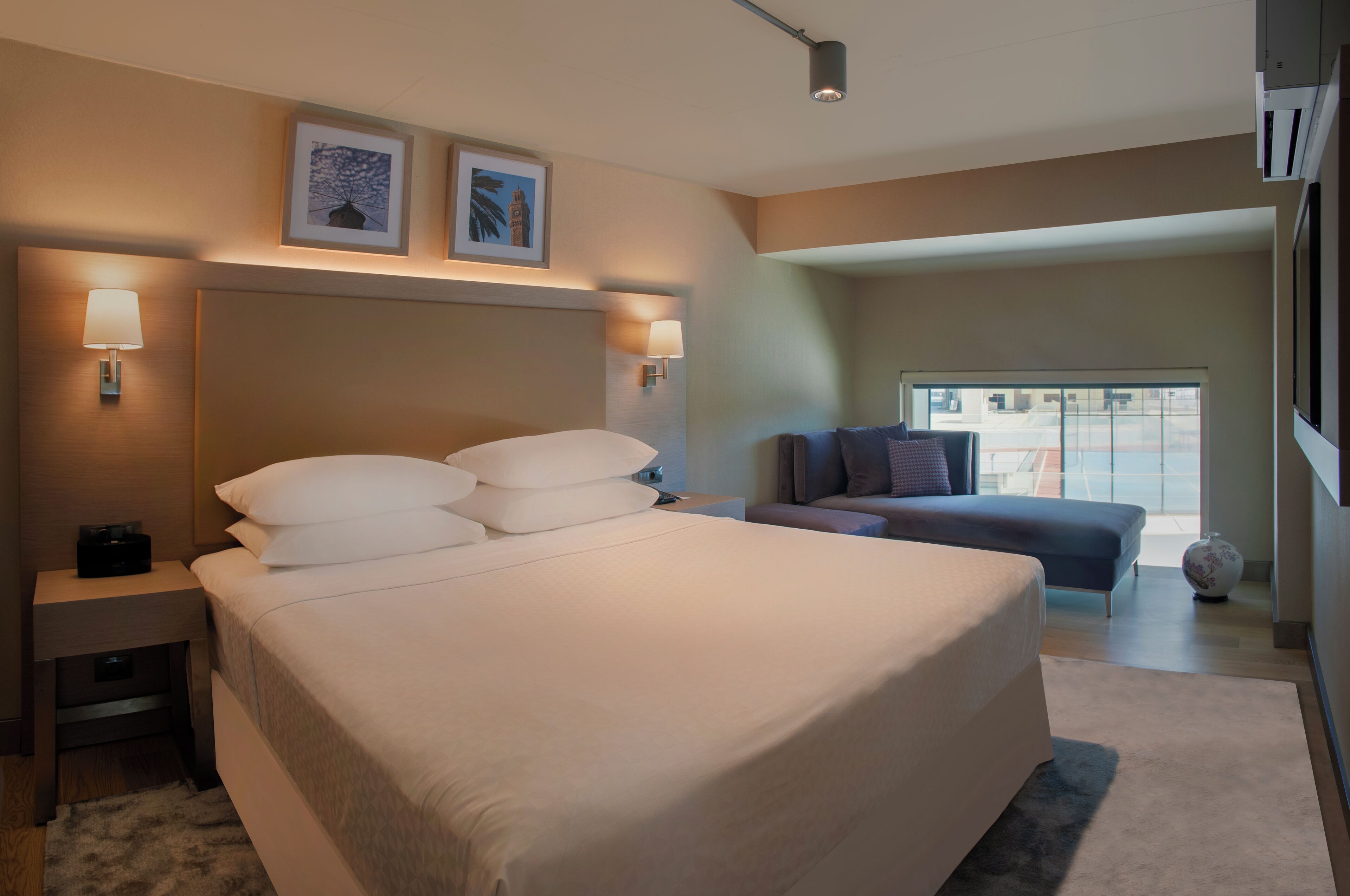 A modern hotel room with a large bed, bedside lamps, a small table, and a sofa.