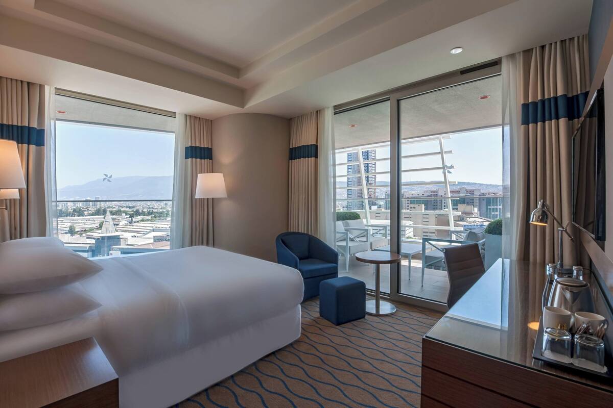 Habitación de hotel con una cama grande, un escritorio, una silla y vistas a la ciudad.