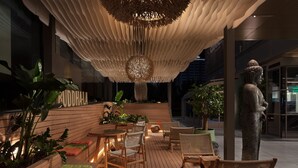 An outdoor seating area with wooden tables and chairs, surrounded by planters with various plants.