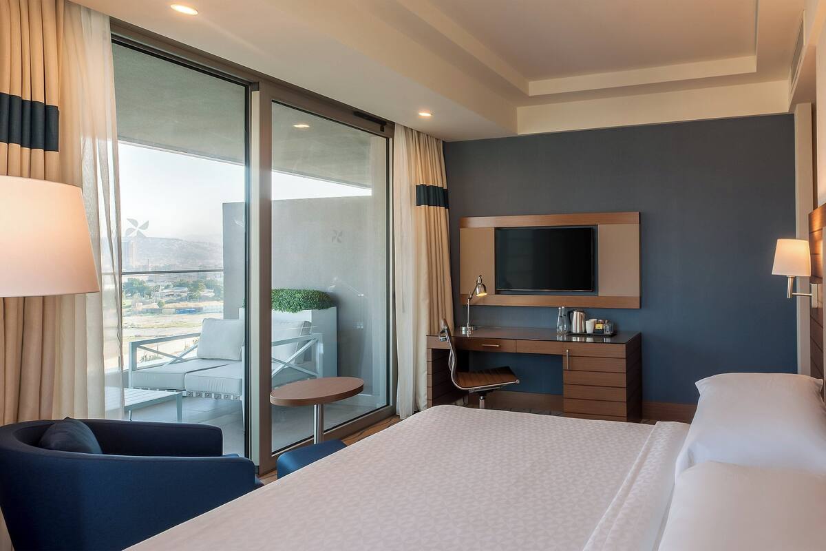 Una habitación de hotel con cama, escritorio, silla, televisión y balcón con vistas.
