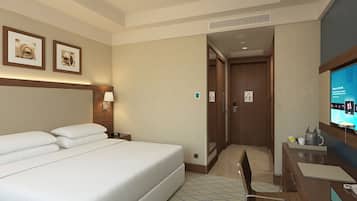 Habitación de hotel con una cama grande, un escritorio con silla, televisión y una puerta que da a otra habitación.