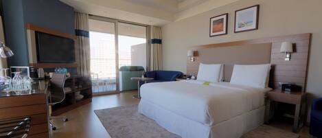 A hotel room with a large bed, a desk with a computer, a TV, and a view of the city.