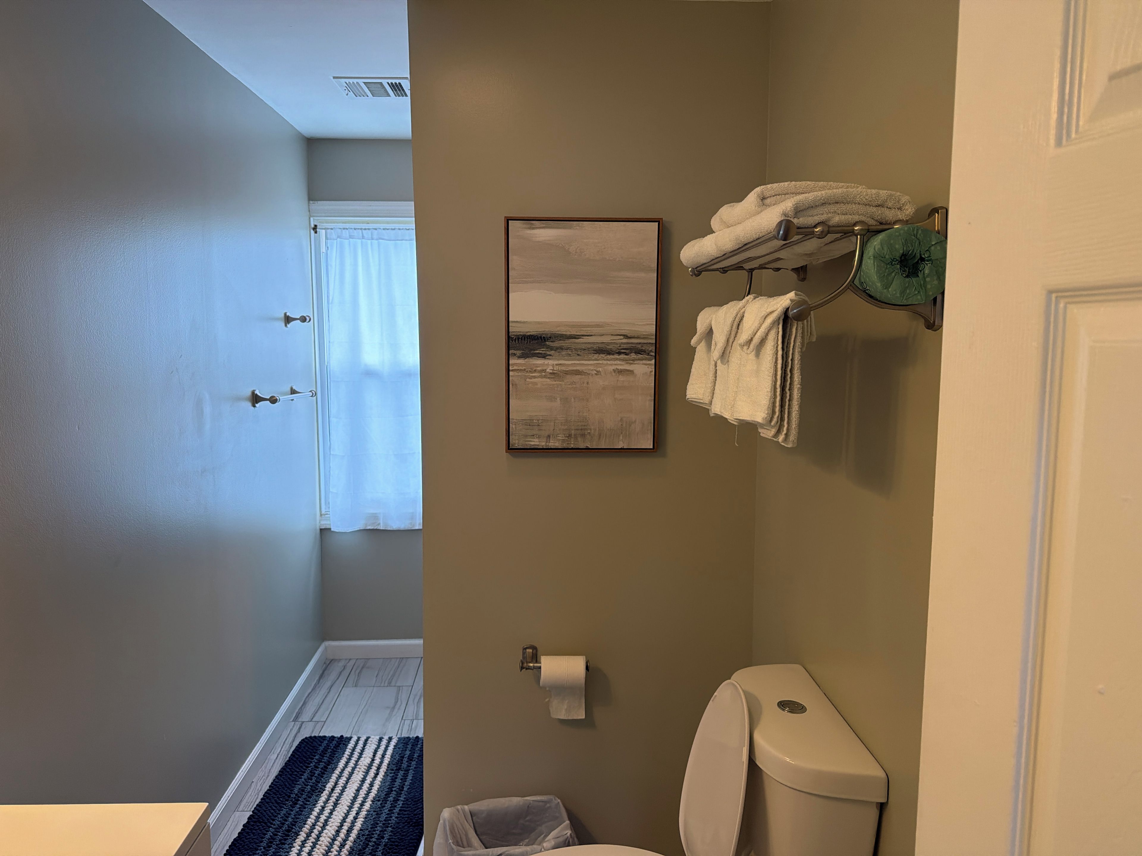 Een badkamer met een toilet, een handdoekhouder, een inlijsting en een raam met gordijnen.