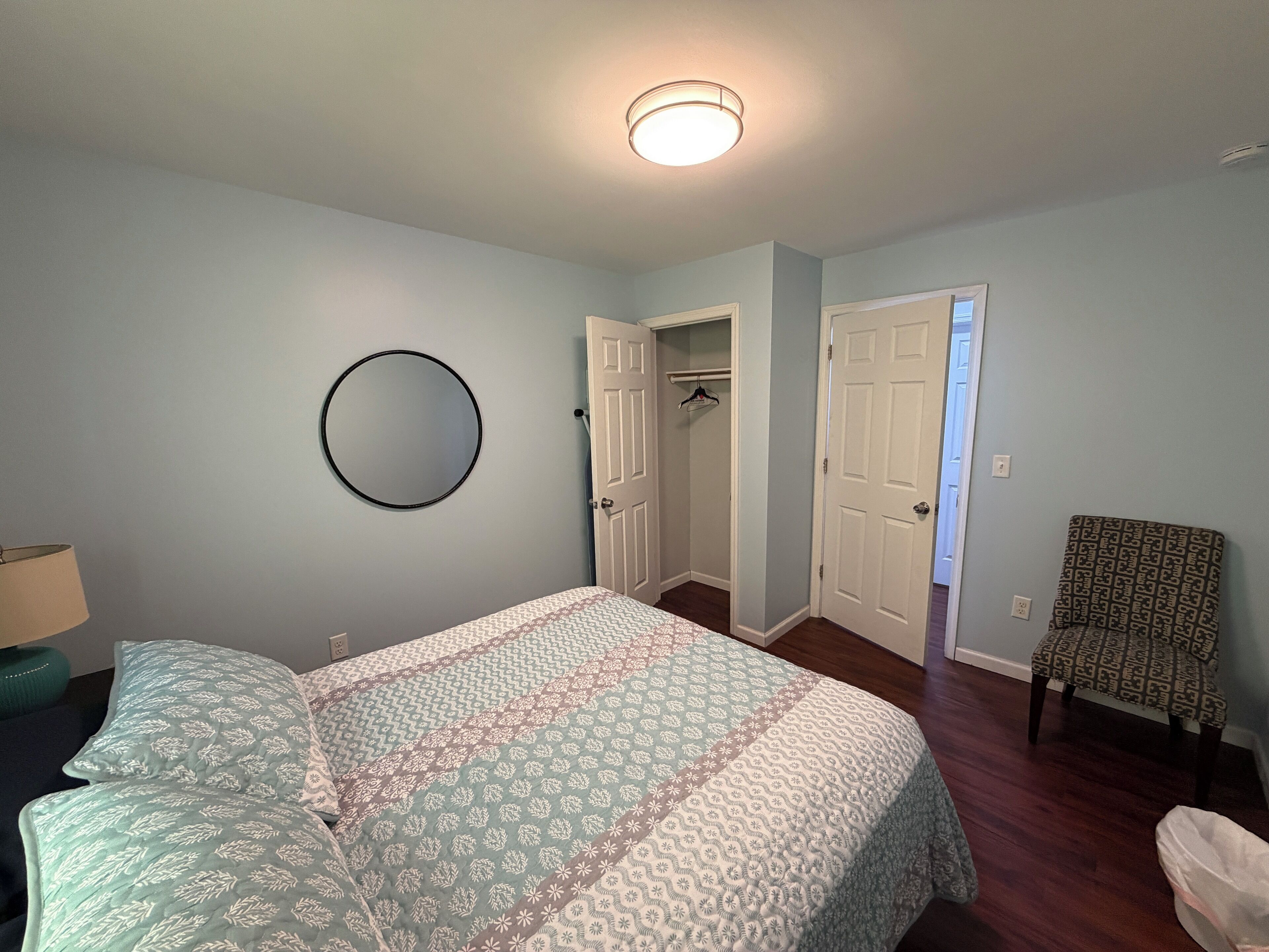 A bedroom with a bed, a circular mirror, a closet, and a chair.