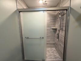 Un box de ducha con paredes de vidrio y una puerta de vidrio satinado, un perchero y un cabezal de ducha.