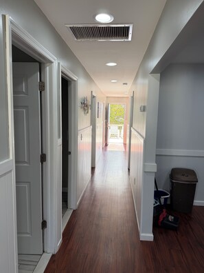 A hallway with wooden flooring, white walls, and a ceiling vent.