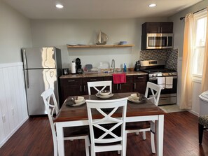 A modern kitchen with a refrigerator, microwave, stove, and sink. There is a dining table with chairs and a red towel on the counter. - JD Apartments (Seaside Heights)