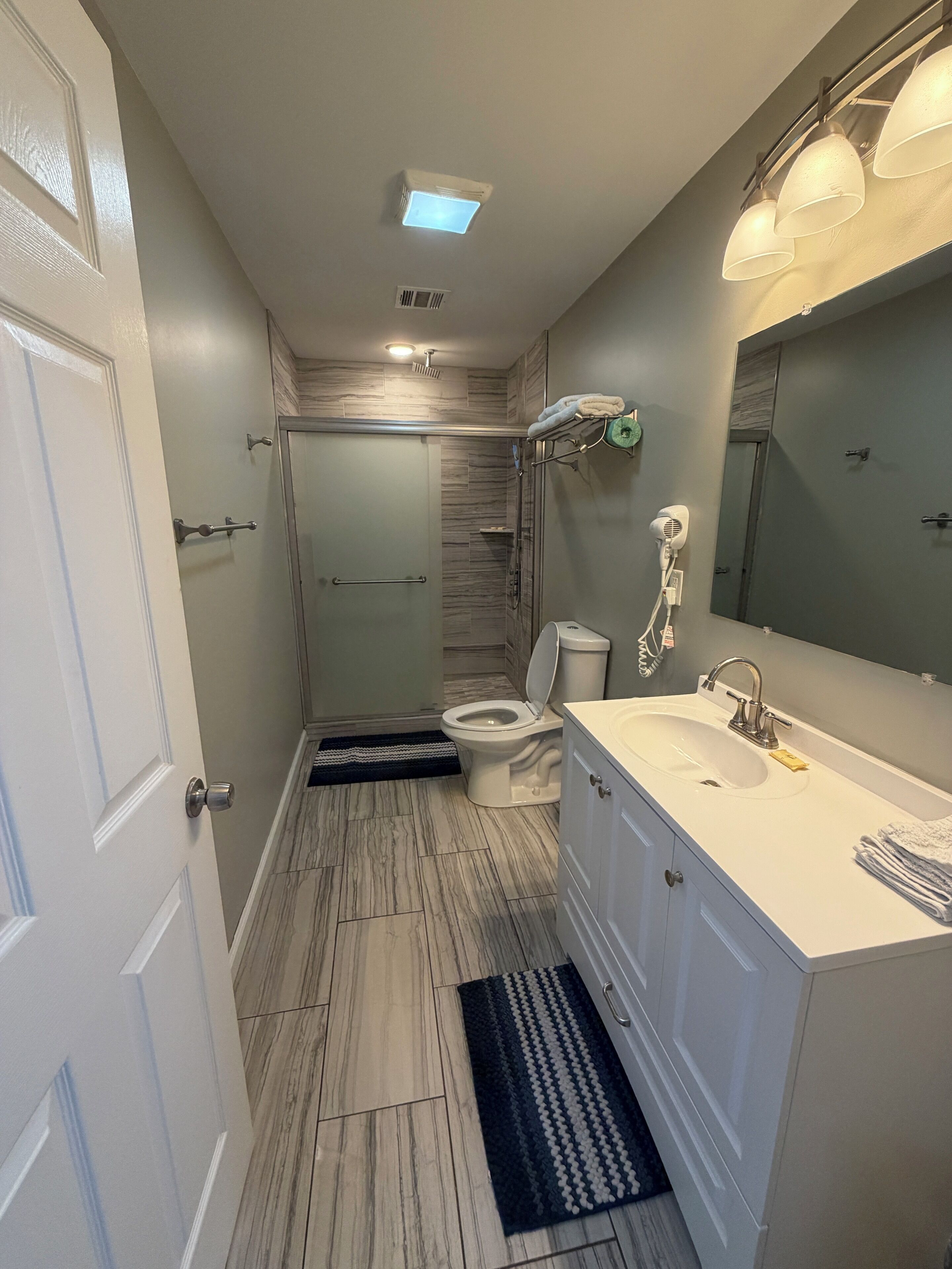 A modern bathroom with a walk-in shower, a toilet, a sink with a mirror, and a hairdryer on the wall.
