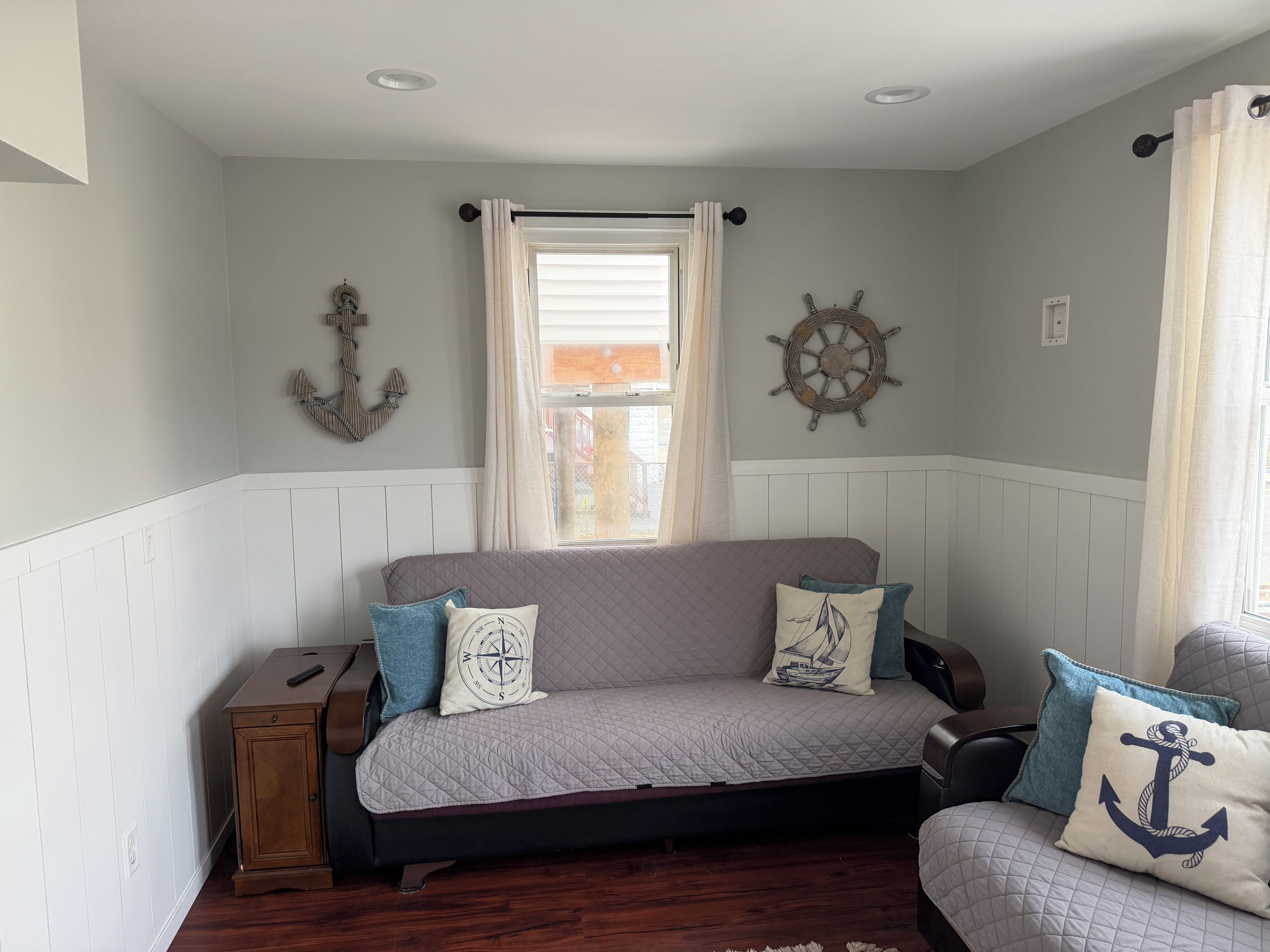 Una habitación acogedora con una cama, un pequeño armario de madera y decoración náutica.
