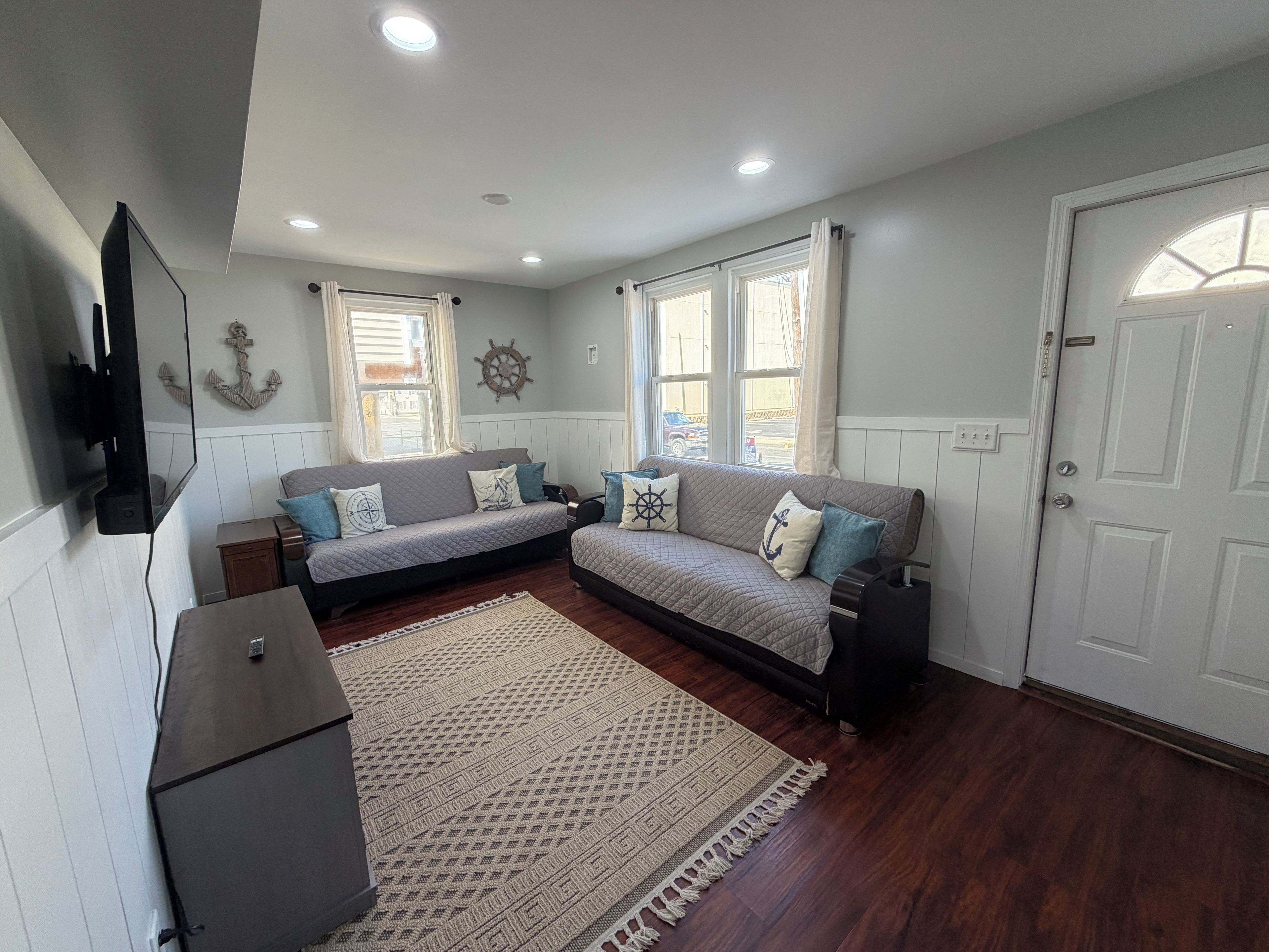 A room with a sofa set, a flat-screen TV, a patterned rug, and a door with a window.