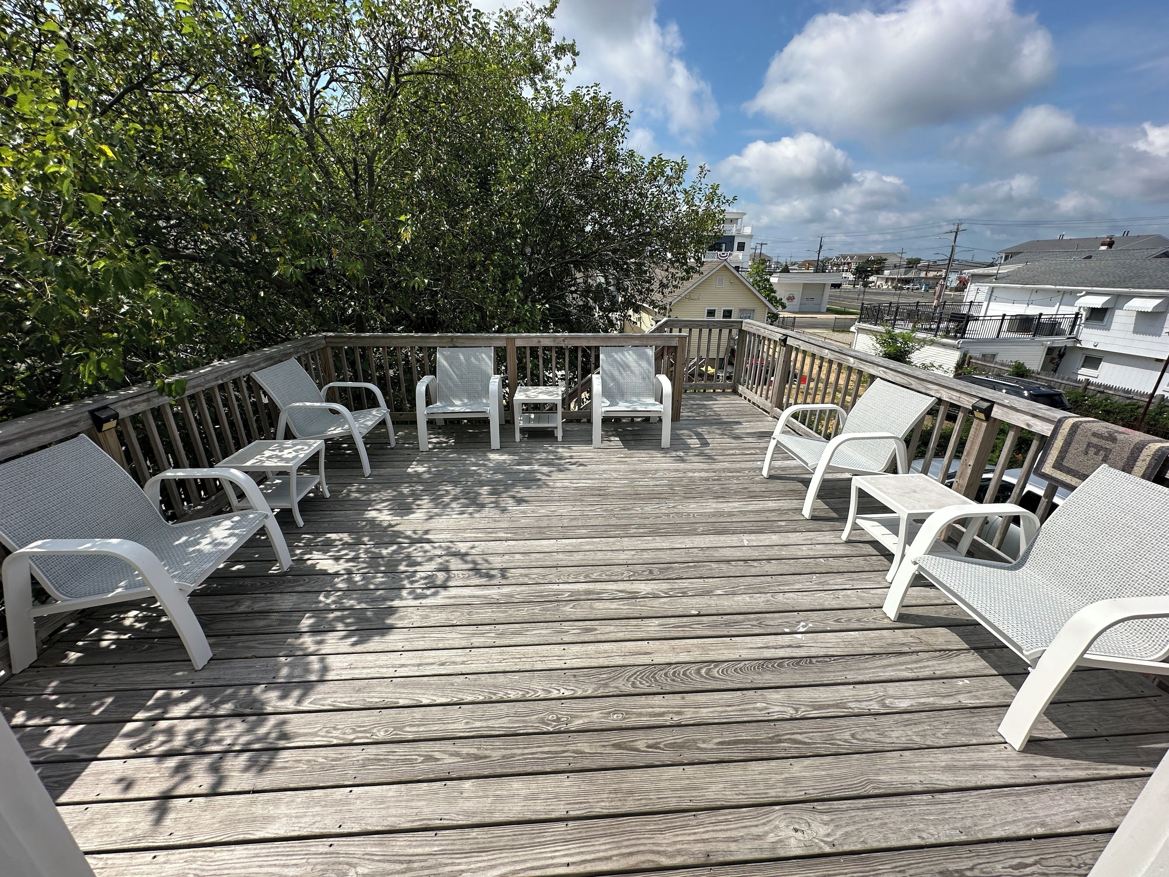 A wooden deck with white chairs and a table, surrounded by trees and buildings.